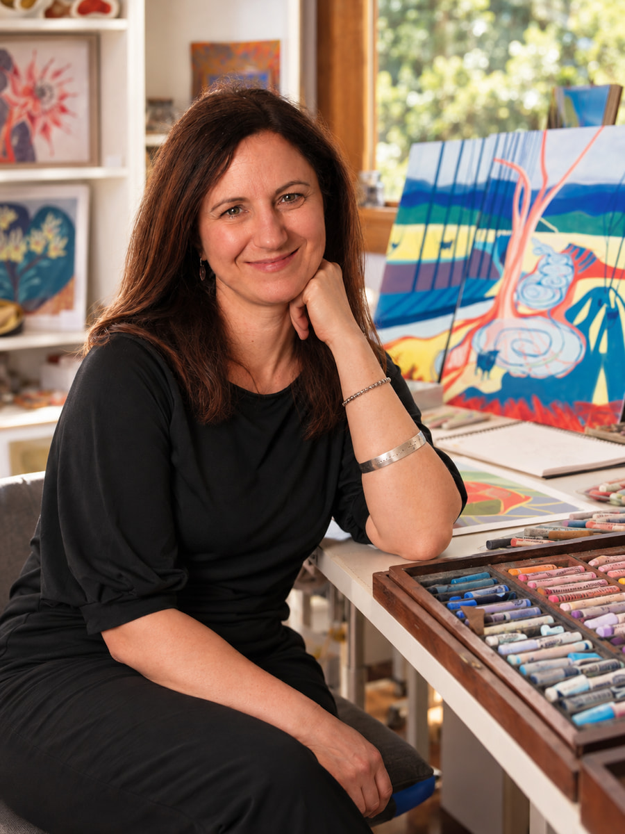 Vivienne Fiori seated in her studio, with pastel colours and drawings beside her.